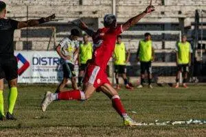 A soccer player in red celebrates a goal with enthusiasm on an outdoor field.