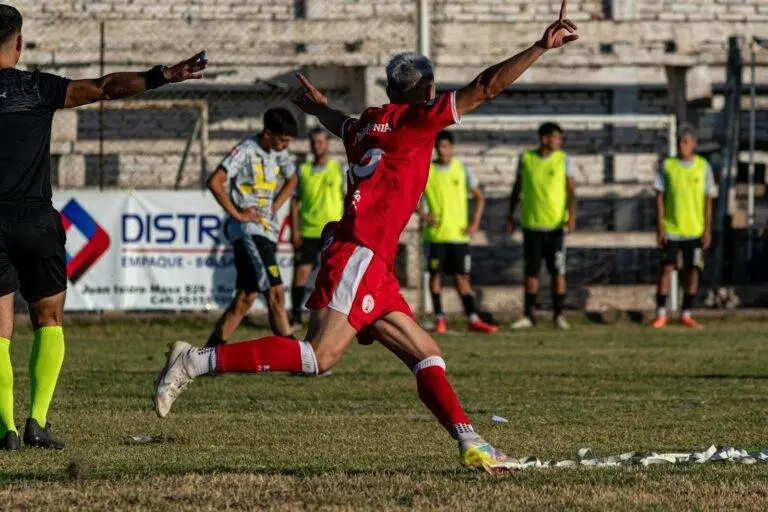 A soccer player in red celebrates a goal with enthusiasm on an outdoor field.