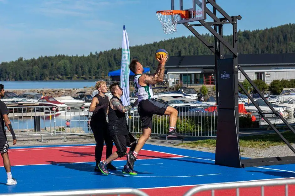 A group of young men playing basketball at an outdoor court near a marina.