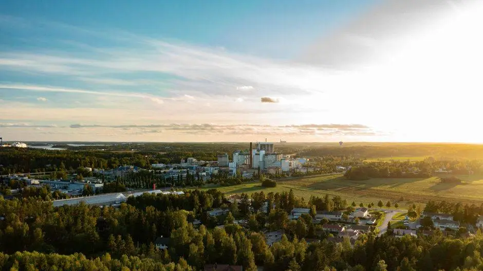 Drone capture of Raisio city with a factory and forested areas at sunrise in summer.