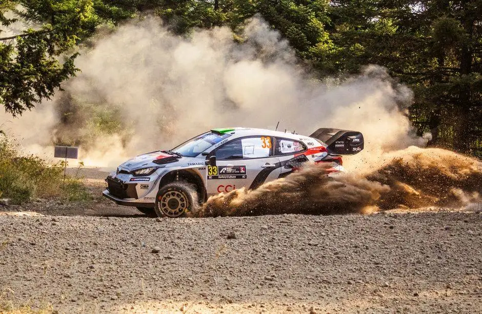 A rally car powers through a dusty road in Pavliani, Greece, kicking up clouds of dust as it navigates the terrain.
