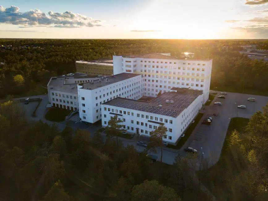 Aerial view of a modern hospital building surrounded by greenery at sunset, illustrating serene healthcare environment.