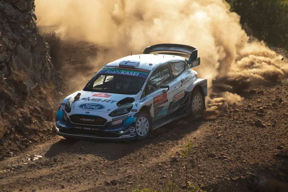 Rally car powers through dusty dirt road corner, showcasing speed and control in an outdoor off-road race.